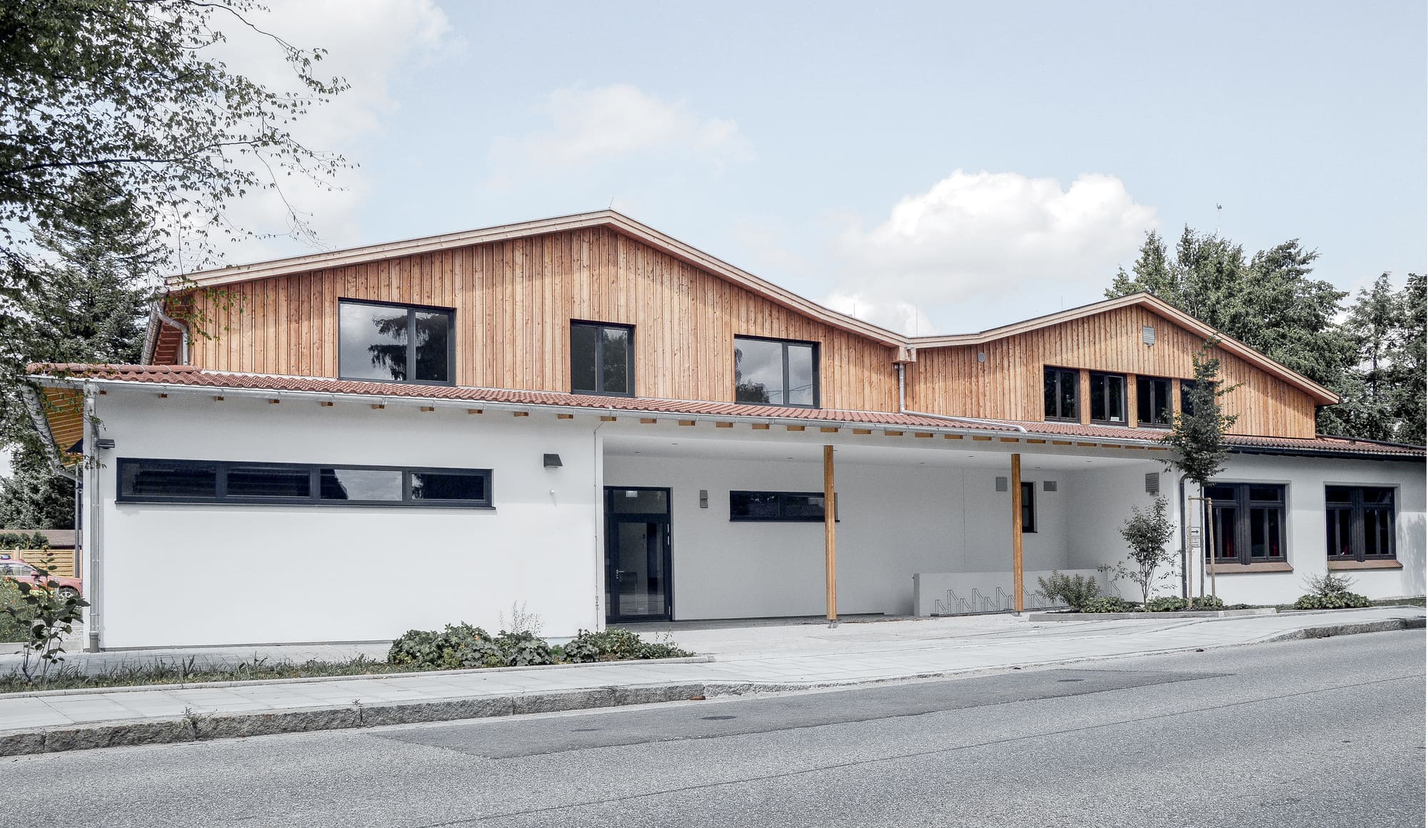 Feuerwehrhaus mit Fahrzeugtoren und holzverkleidetem Obergeschoss – Anbau und Umbau der Feuerwehr Parsdorf